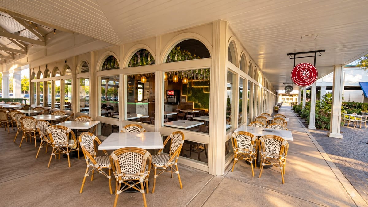The covered patio with white marble tables and woven bistro chairs beside arched windows